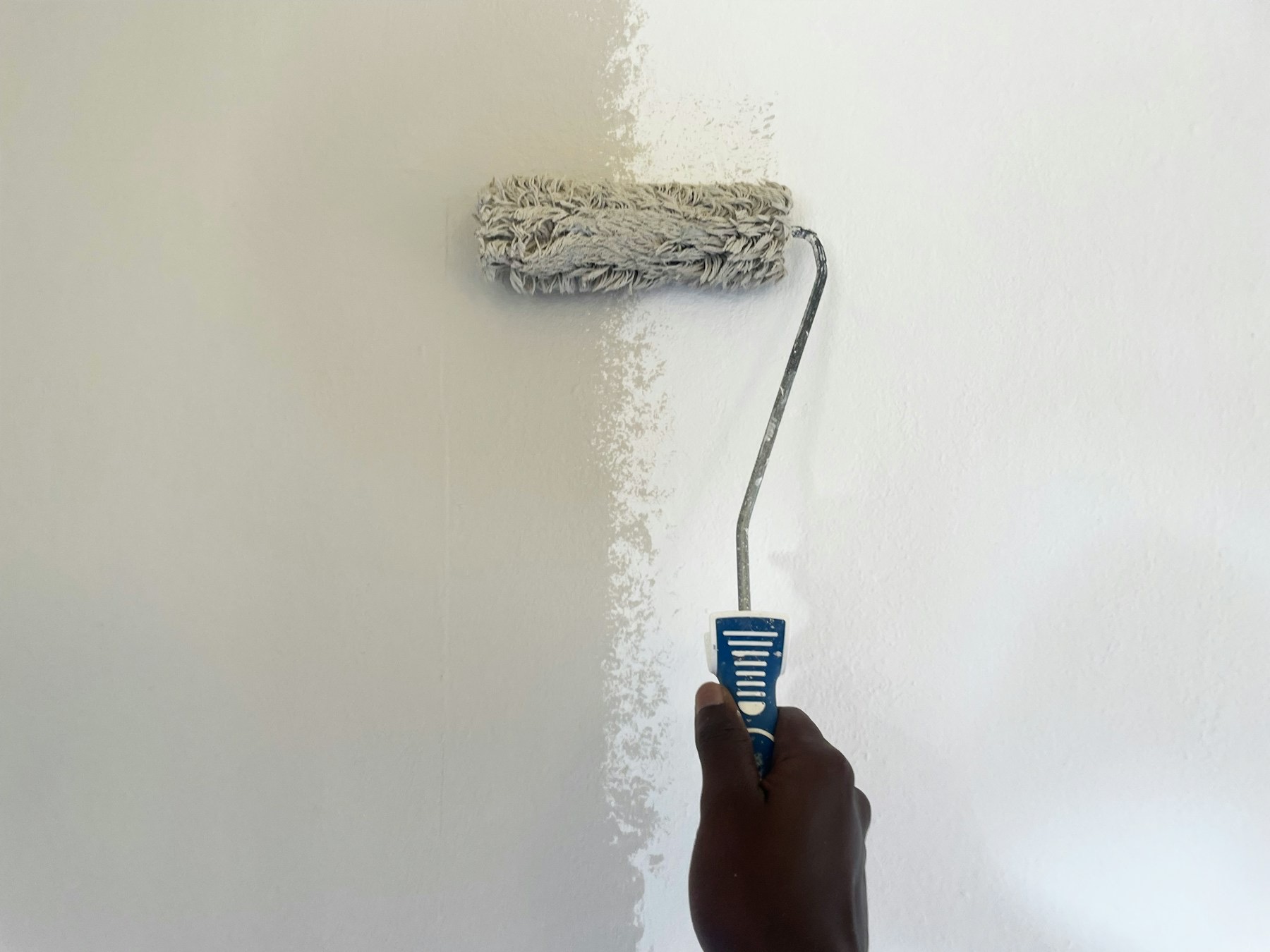 Main passant un rouleau de peinture blanche sur un mur.